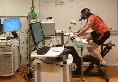 a young woman pedals an exercise bike while wearing a mask to monitor oxygen consumption a young woman pedals an exercise bike while wearing a mask to monitor oxygen consumption